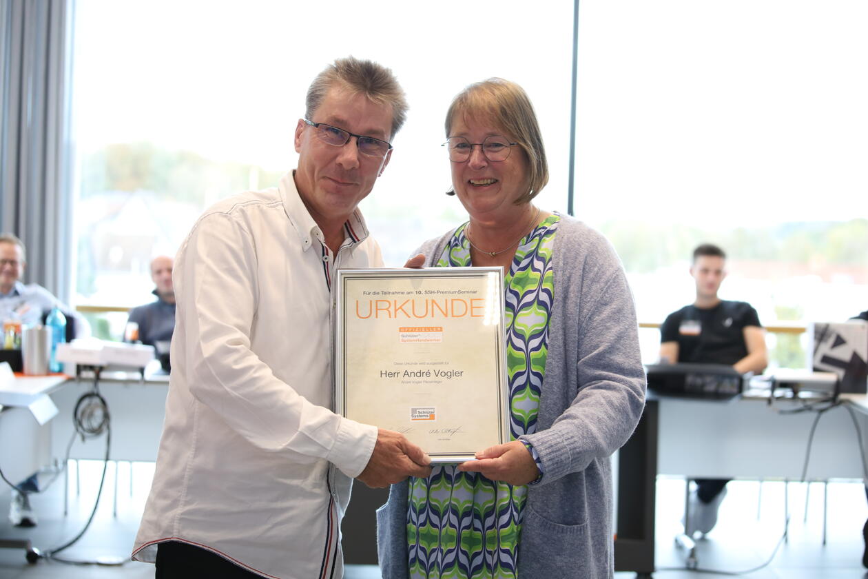 Anke Kuhaupt, Leiterin CLM bei Schlüter-Systems, überreicht André Vogler die Urkunde für die zehnmalige Teilnahme an einem Premiumseminar für Schlüter-SystemHandwerker.