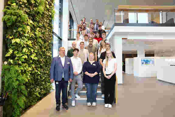 Geschäftsführer Udo Schlüter, die Ausbilderinnen und Ausbilder sowie die neuen Auszubildenden auf der Treppe im unternehmenseigenen Schulungszentrum