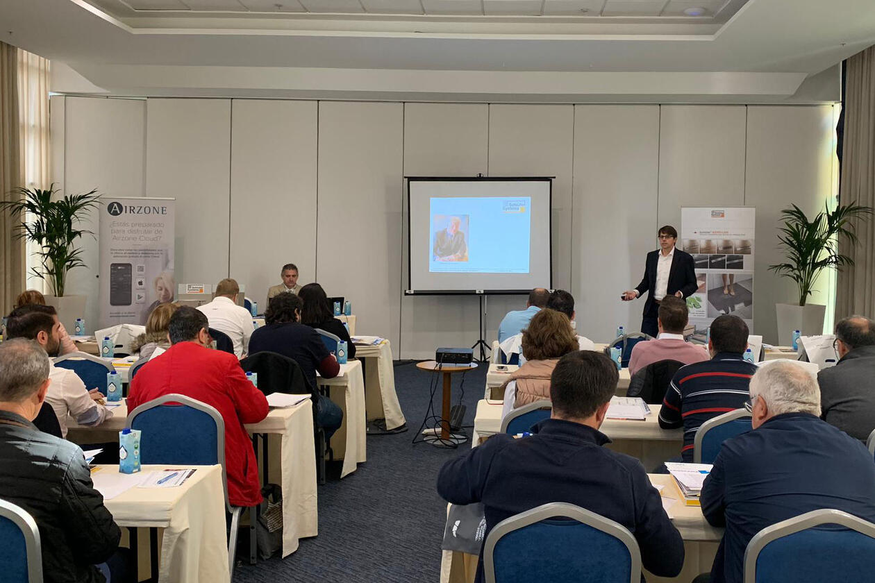  Los participantes en un seminario están sentados en una sala, con la vista dirigida hacia una presentación que se proyecta en una pantalla, mientras un hombre imparte una conferencia.