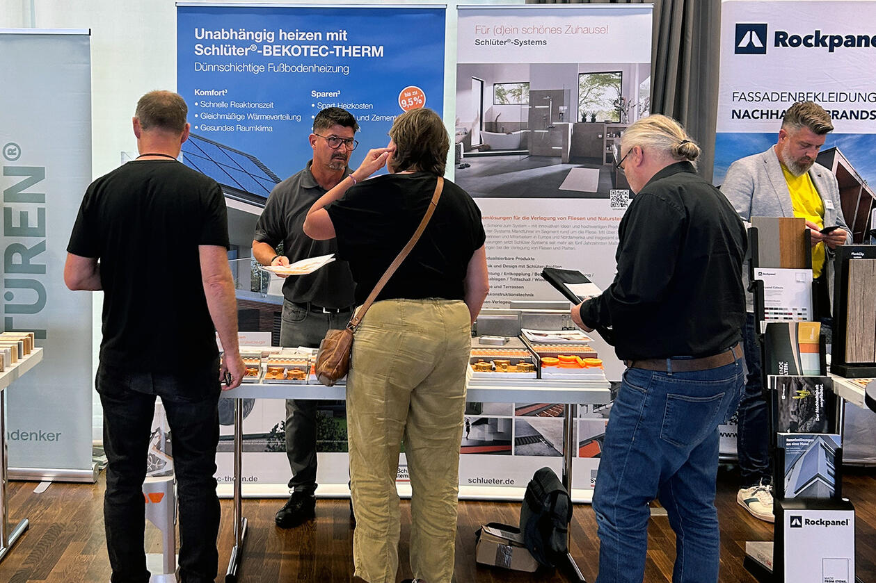 Schlüter-Systems war als Gastgeber ebenfalls mit einem Stand zu BEKOTEC-THERM vertreten. Drei Personen stehen an einem Ausstellungsstand und lassen sich von einem Mann zu BEKOTEC-THERM informieren.