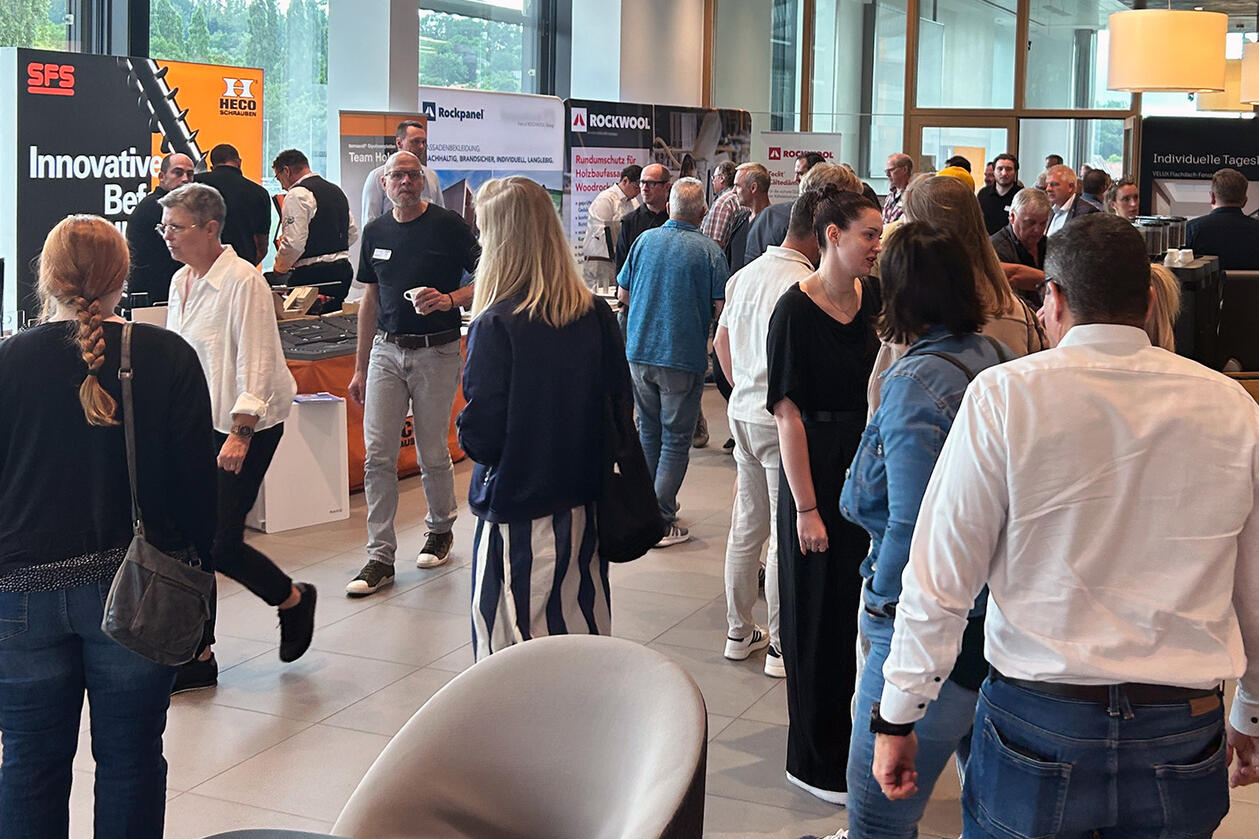 Die Gäste informierten sich über Neuheiten der Holzbaubranche. ROCKWOOL selbst hatte auch einen Stand in der WorkBox. Gäste stehen vor Ausstellungsständen im Schulungszentrum von Schlüter-Systems.