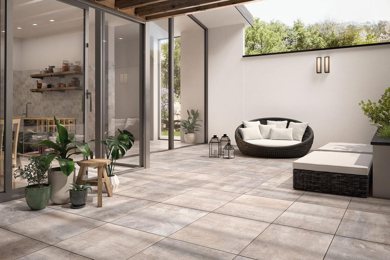 Außenansicht einer hochmodernen Terrasse als Erweiterung des Wohnbereichs mit hellgrauen Fliesen, bequemen Loungemöbeln und Pflanzen sowie Dekorationsartikeln.