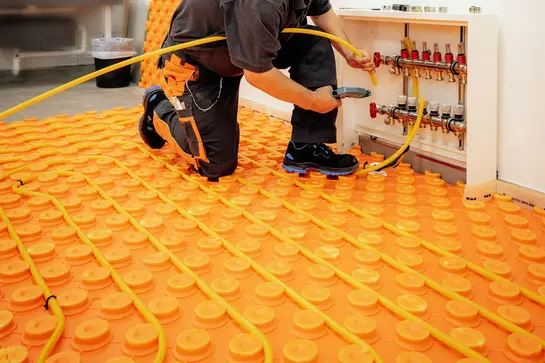 Řemeslník zkracuje topnou trubku na délku potřebnou pro topný okruh a pokládá ji do oranžové desky s výlisky BEKOTEC od firmy Schlüter-Systems.