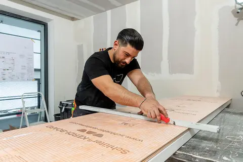Řemesln&iacute;k firmy Schl&uuml;ter-Systems řeže desku Schl&uuml;ter-KERDI-BOARD odlamovac&iacute;m nožem.