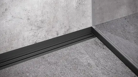 Hjørne i et gråt flisebelagt brusebad med bruserende, faldkile og vægtilslutningsprofil i mat sort