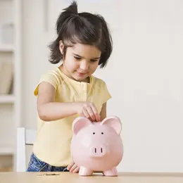 Little dark-haired girl putting money into a piggy bank.