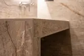 Close-up of a corner of a vanity unit with brown marbled tiles and brown textured finishing profiles