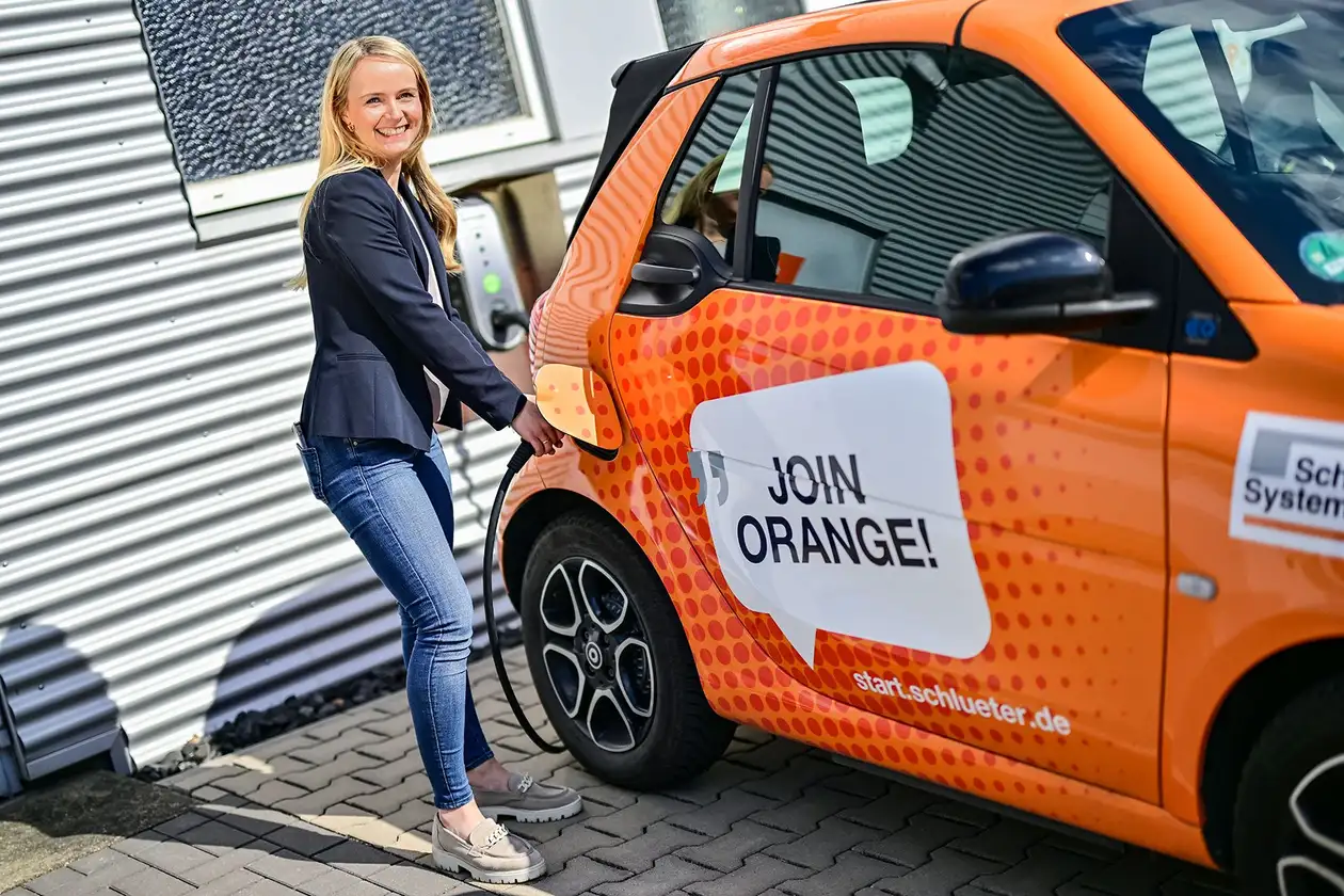 Female employee charges the Schlüter-Systems apprentice Smart car at an electric charging column.