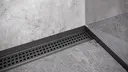 A corner in a grey tiled shower with shower channel, sloped profile and wall connecting profile in matte black