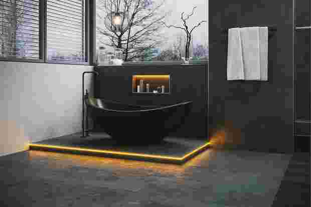 Dark bathroom with free-standing bathtub and an illuminated KERDI-BOARD-NLT wall niche.