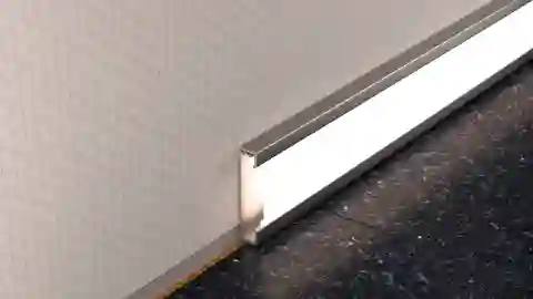 Warm white illuminated Schlüter-DESIGNBASE-QD profile as skirting board on the floor covering
