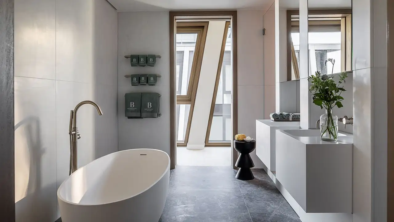 Bathroom in ‘The Broadway’ with free-standing bathtub and two wall-mounted washbasins.