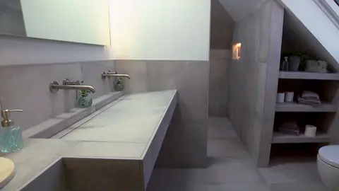 View of the bathroom with sloping roof, double washbasin unit, tiled built-in shelving and illuminated wall niche