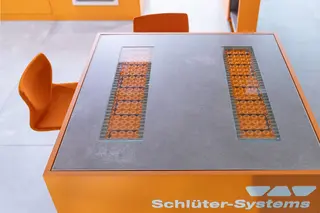 Elektrische Boden- und Wandheizung in einem Tisch verbaut, an dem zwei orangefarbene St&uuml;hle stehen.