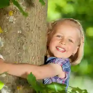 Kleines blondes Mädchen umarmt einen Baum.