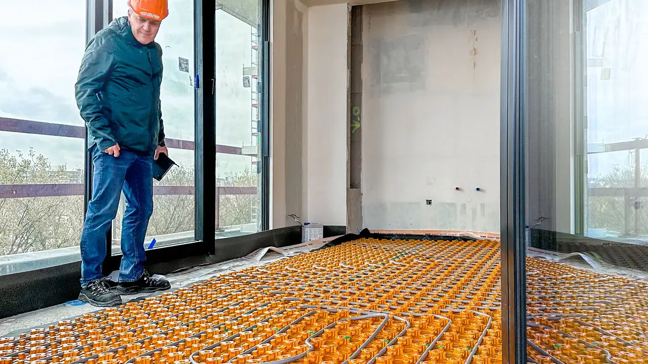 Ein Mann Schutzhelm blickt pr&uuml;fend auf die verlegte BEKOTEC-THERM Matte mit Heizrohren in einem Raum der City Dox