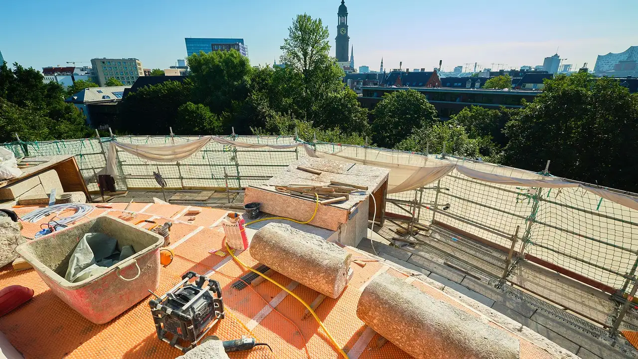 Stufen des Bismarck-Denkmals ohne Natursteinbekleidung mit darunter angebrachter Schlüter-TROBA-PLUS 8G. Darauf liegen Steinsäulen und Werkzeuge. Von dort zu sehen die Aussicht auf die Stadt  mit großem Kirchturm.