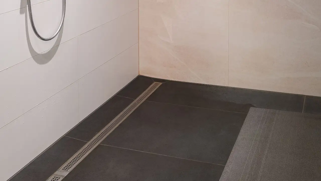 Die fertig gefliesten Duschen im Vereinsheim mit KERDI-LINE Duschrinne, dunkelgrauen Boden- und wei&szlig;en Wandfliesen