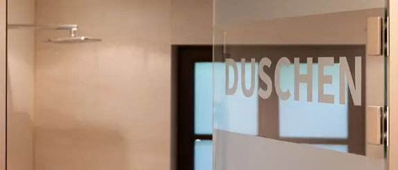 Blick in den frisch renovierten Duschbereich von Tennis Hirschau durch eine halb ge&ouml;ffnete Glast&uuml;r