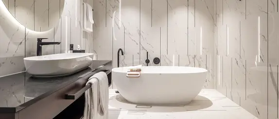Badezimmer im Hotel Steigenberger Hof mit wei&szlig;en Marmorfliesen, freistehender Wanne und Schl&uuml;ter-LIPROTEC Lichtprofilen in der Wand