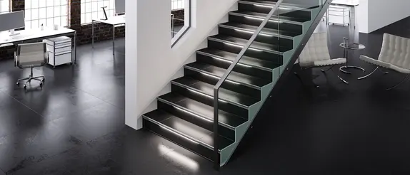 Gro&szlig;z&uuml;giges B&uuml;roloft mit wei&szlig;en Lounge-M&ouml;beln, das in der Mitte durch eine wei&szlig;e Trennwand geteilt ist, vor der eine beleuchtete Treppe mit Metallgel&auml;nder nach oben f&uuml;hrt.