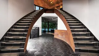 Beleuchtete, in einem Bogen geschwungene Doppeltreppe, die rechts und links in einem Atrium in die obere Etage f&uuml;hrt