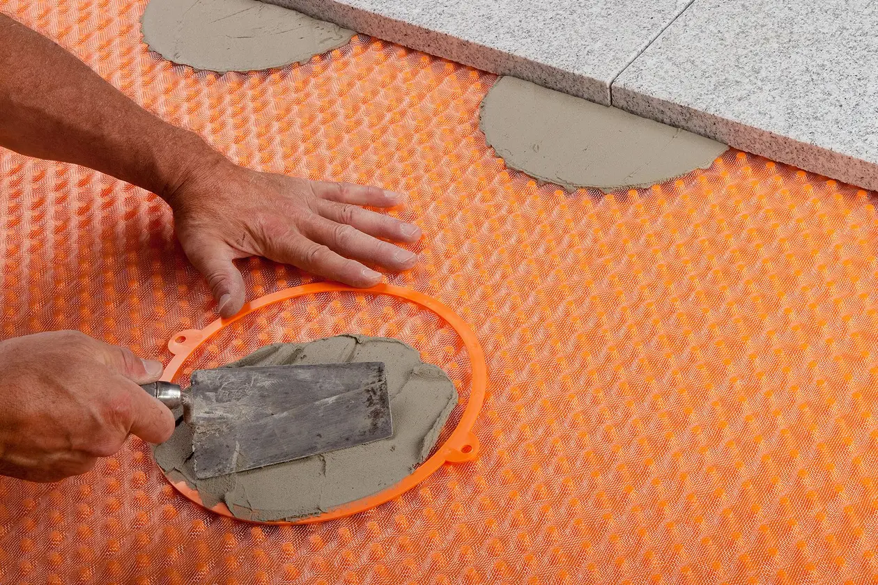 Ein Schalungsring auf einer Drainagematte wird mit Mörtel befüllt und an den Ecken mit Platten belegt
