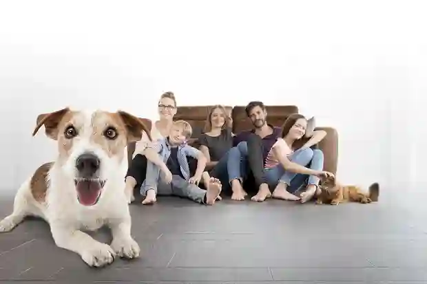 Eine Gruppe von fünf Menschen, einem Hund und einer Katze sitzen auf einem dunklen Fliesenboden. 