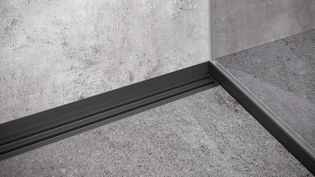 Grau geflieste Rückwand einer Dusche mit schwarzer Duschrinne und zusätzlichen Duschprofilen