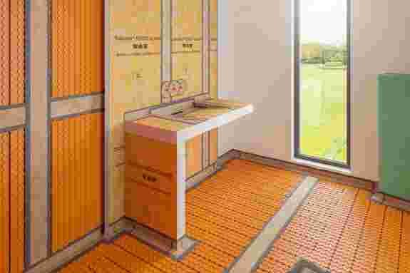 Orangener Verlegeuntergrund in einem Badezimmer mit Entkopplungsmatte, Heizrohren und einem Waschtisch aus KERDI-BOARD Platten