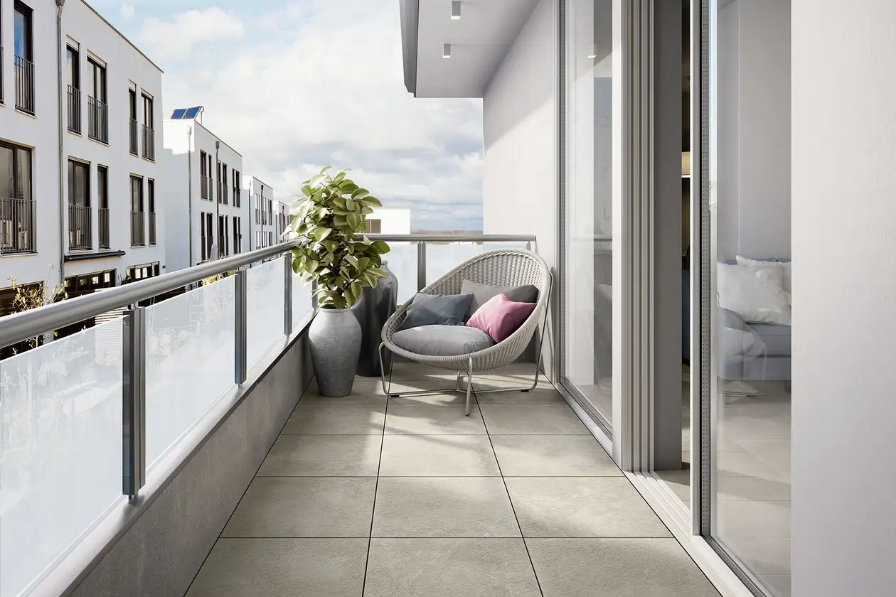 Hellgrau gefliester Balkon mit milchigem Sichtschutz, im hinteren Bereich eine Planze und ein Lounge-Sessel