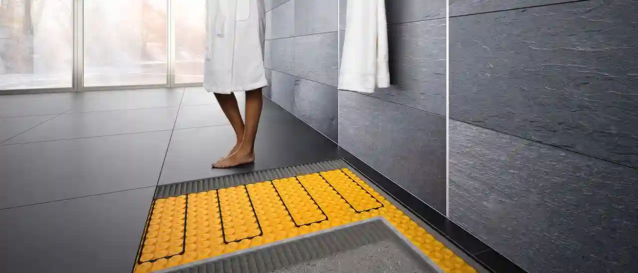Eine Person im Bademantel steht auf Badezimmerfliesen, die mit DITRA-HEAT-E beheizt sind