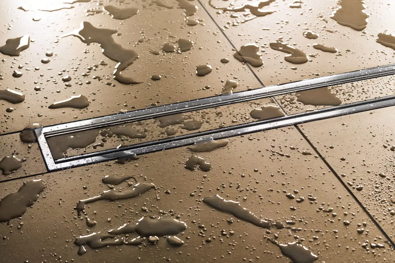 Auf gro&szlig;formatigen beigen Fliesen stehen Wasserpf&uuml;tzen und -tropfen