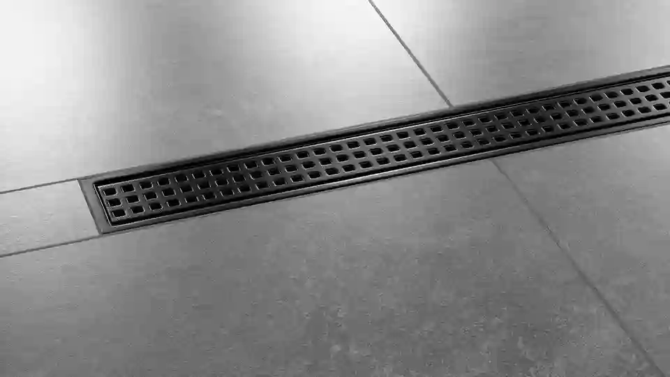Zu sehen ist eine Nahaufnahme eines dunkelgrau gefliesten Duschbodens mit der mittig installierten Duschrinne Schlüter-KERDI-LINE-B im Design SQUARE in der TRENDLINE-Farbe graphitschwarz matt
