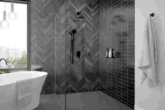 Schlüter-Systems Duschrinne KERDI-LINE und Duschablage SHELF in MGS Graphitschwarz matt eingebaut in einem modern gestalteten Badezimmer mit dunkelgrauen Fliesen, bodengleicher Dusche, freistehender Badewanne und schwarzen Armaturen.