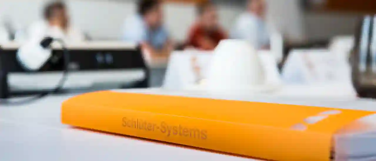 Ein orangener Hefter mit Aufschrift Schlüter-Systems liegt auf einem Tisch