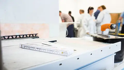 Ebene Arbeitsfläche in eimem Schulungsraum mit Profilkante, Zollstock, Kelle, Spachtel und Schulungsteilnehmern im Hintergrund
