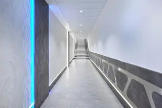 Hell beleuchteter Flur mit blauen Lichtakzenten und einer Treppe mit beleuchteten Stufen am Ende des Ganges