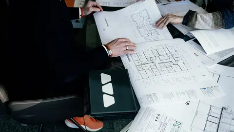 Zwei Personen begutachten Grundrisspläne eines Mehrfamilienhauses auf einem Tisch