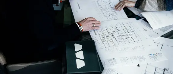 Auf einem Tisch ausgebreitete Grundrisszeichnungen eines mehrstöckigen Gebäudes