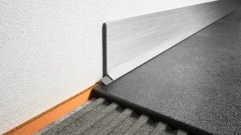 Nahaufnahme eines Boden-Wand-Übergangs mit einem Schlüter-DESIGNBASE-SL Sockelprofil in gebürstetem Aluminium