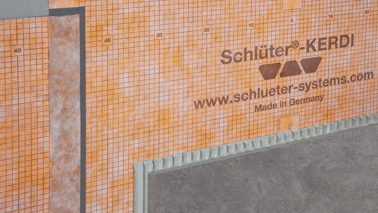 Die orangene Schlüter-KERDI-200 Abdichtungsbahn an einer Wand verklebt und teilweise schon mit einer grauen Fliese belegt