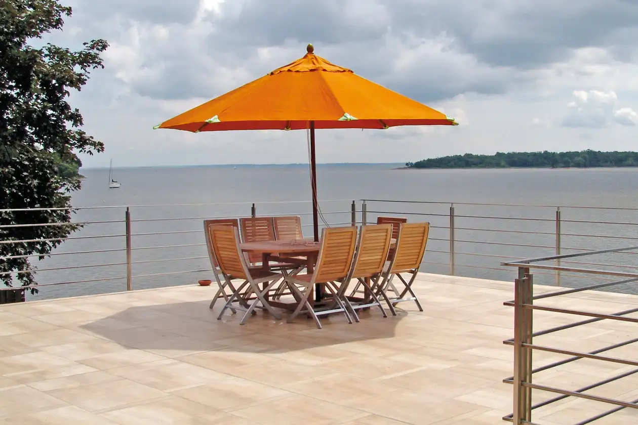 Dachterrasse mit Blick auf einen See, in der Mitte eine Sitzgruppe mit orangenem Sonnenschirm