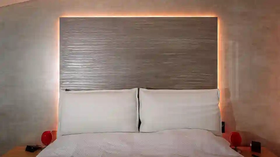 Ein Schlafzimmer mit Bett und dahinterliegender, beleuchteter Wandscheibe