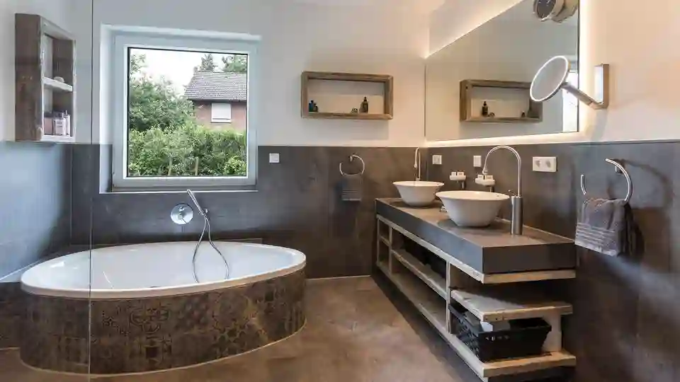 Foto des renovierten Badezimmers mit Wanne, Waschtischanlage und beleuchtetem Spiegel.