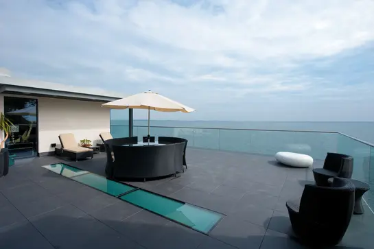 Blick &uuml;ber eine Dachterrasse mit Lounge-M&ouml;beln aufs Meer