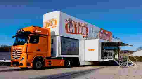 Außenansicht des Schlüter-WorkBox ON TOUR-Trucks auf einem Parkplatz mit Multimedialeinwand.