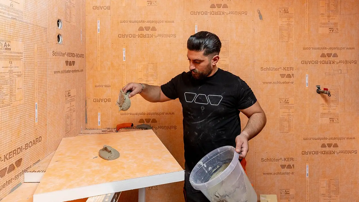 Ein Handwerker verteilt Mörtel auf orangenen KERDI-BOARD Verlegeplatten