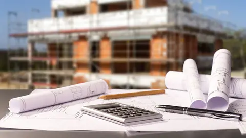 Planos y calculadora de bolsillo sobre una mesa con una obra de fondo