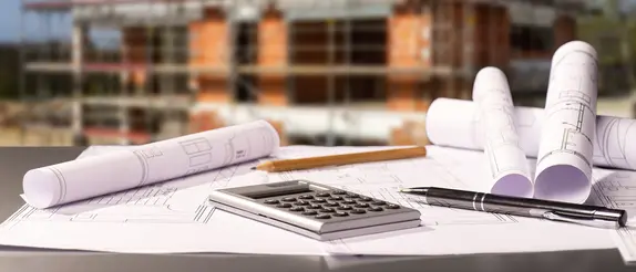 Planos y calculadora de bolsillo sobre una mesa con una obra de fondo